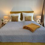 Ein Bett mit gelbem Kopfteil, grauer Decke und Kissen. Beide Nachttische haben Lampen.