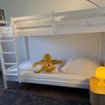 Schlafzimmer mit weißem Doppelstockbett, gelber Tischlampe und Plüschoktopus.