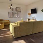 Wohnzimmer mit gelben Sitzmöbeln, Wandbildern und Fernseher.