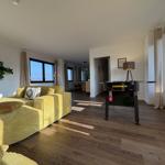 Wohnbereich mit gelbem Sofa und Tischfußball. Holzboden und große Fenster.