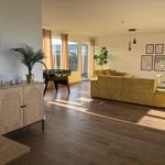 Wohnzimmer mit gelbem Sofa, Holzboden und Fenster zur Terrasse.