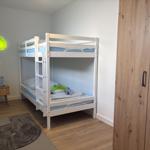 Zimmer mit Doppelstockbett, Kleiderschrank und Wandlampen in Form von Blättern.