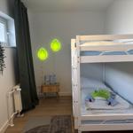 Zimmer mit Doppelbett, Nachttisch und Fenster mit Vorhängen.