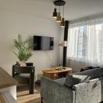 Wohnbereich mit Sofa, Sessel, TV und Fenster mit Gardinen.