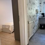 Schlafzimmer mit Bett und angrenzender Küchenzeile mit Kaffeemaschine.