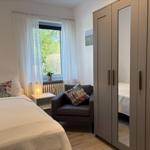 Schlafzimmer mit Bett, Kleiderschrank und Fenster mit Blick auf Grün.