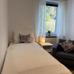 Ein Schlafzimmer mit Bett, Sessel und Fenster. Auf dem Fensterbrett steht eine Pflanze.