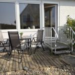 Terrasse mit Tisch und Stühlen vor einem Haus mit weißen Wänden und Glasfront.