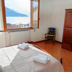 Schlafzimmer mit Blick auf See und Berge. Bett, Stuhl und Schrank sind sichtbar.