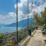 Terrasse mit Blick auf See und Berge, Flaggen und Bäume sichtbar.