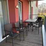 Terrasse mit Tisch und vier Stühlen, Holzboden und roter Wand.