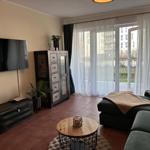 Wohnzimmer mit Sofa, TV und Balkon. Holztisch und Schrank sind sichtbar.