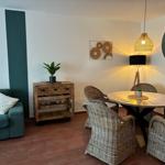 Essbereich mit runden Tisch und Stühlen. Sofa, Wanduhr und Beleuchtung sind sichtbar.