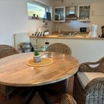 Runder Holztisch mit Strohstühlen und Küchenbereich im Hintergrund.