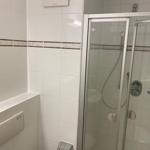 Bad mit Dusche und Toilette. Weiße Fliesen mit dekorativer Bordüre.