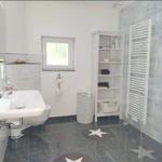 Badezimmer mit Dusche, Waschbecken und Regal. Fliesenboden und Fenster.