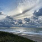 Strand mit Dünen, Meer und bewölktem Himmel mit Sonne.