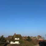 Haus mit strohgedecktem Dach auf grüner Anhöhe unter blauem Himmel.