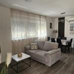 Wohnzimmer mit Sofa, Tisch und Essbereich. Holzboden und Fenster mit Vorhängen.