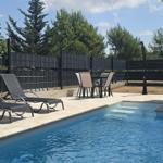 Pool mit Liegen und Tisch im Garten mit Zaun und Bäumen.