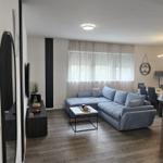 Wohnzimmer mit grauem Sofa, Holzboden und Fenster mit Vorhängen.