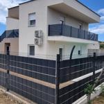 Moderne zweistöckige Villa mit Balkon und schwarzer Umzäunung.