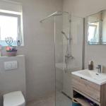 Badezimmer mit Dusche, Waschbecken und Toilette. Blauer Teppich und Spiegel.