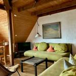 Wohnbereich mit grünem Sofa, Holzboden und weißer Wand. Esstisch und Fernseher sichtbar.
