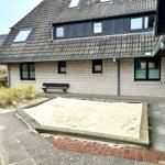 Haus mit Sandkasten und Steinplattenhof. Dach mit Dachfenstern und Ziegeln.