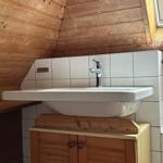 Waschbecken mit Holzunterschrank und Fliesenwand in Dachschrägen