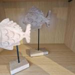 Zwei hölzerne Fischdekorationen auf Ständern in einem Schrank
