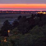 Abendblick auf eine Lichterkette am Horizont über Wiesen und Bäumen.