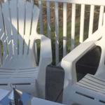Zwei weiße Sessel und ein Tisch auf einer Terrasse mit Geländer.