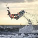 Kitesurfer vollführt eine Sprungaktion über das Meer bei Sonnenuntergang.