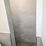Dusche mit grauen Fliesen und dunklem Boden, ein Handtuch liegt darauf.