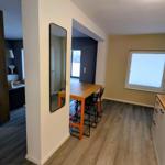 Küche mit Holzplatte und Stuhl. Tisch mit Stühlen. Spiegel an der Wand. Tür zum Schlafzimmer.