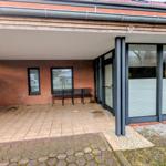 Terrasse mit Sitzbank, Glasfront und Backsteinmauer. Eingang mit Rollladen.