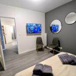 Schlafzimmer mit Bett, Fernseher und zwei Stühlen. Zwei runde Spiegel an der Wand.