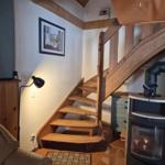 Wooden staircase leads upstairs. Fireplace and wall picture are visible.