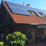 House with solar panels on roof, terrace with garden furniture and plants.
