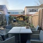 Terrace with seating group, grill, and small wooden house in background.