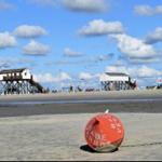 Beach with tidal flats, red buoy, and wooden beach huts in the background.