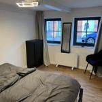Bedroom with bed, wardrobe, mirror and windows. Wooden floor and black furniture.