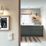 Küche mit dunklen Schränken, Fenster und Teppichboden. Wandbild und Wandlampe sichtbar.