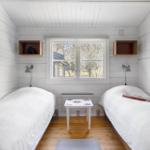 Two beds, window, table, and wall shelves in a room with white wood.
