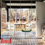 Patio with swings, table and chairs, woodpile and forest view.