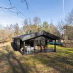 Wooden cabin with terrace, grill area, and trampoline in the woods.