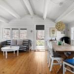 Living and dining area with wooden floor, white wall paneling, and table with chairs.