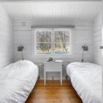 Two beds, one window, wooden floor, white walls.