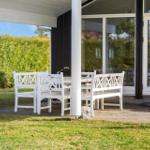 White outdoor area with table and chairs under cover. Background: green hedge area.